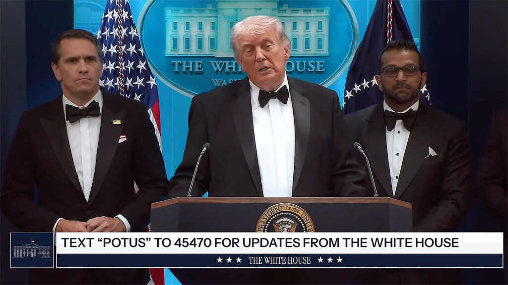 Donald Trump w smokingu przemawia z Białego Domu w nocy z 25 na 26 kwietnia 2026, godziny po strzelaninie w hotelu Washington Hilton podczas kolacji White House Correspondents' Dinner. Po prawej Trumpa pełniący obowiązki prokuratora generalnego Todd Blanche, po lewej dyrektor FBI Kash Patel.