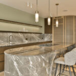 A kitchen with a marble counter top and three chairs