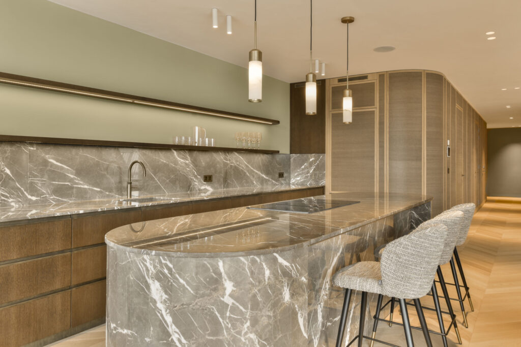 A kitchen with a marble counter top and three chairs