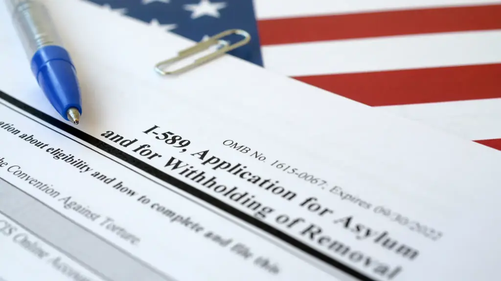Pusty formularz I-589 (wniosek o azyl) leży na fladze USA obok niebieskiego długopisu