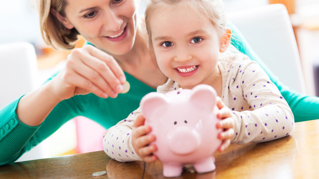 Girl dropping a coin into a piggy bank with her mother – Social Security benefits for a child in Poland