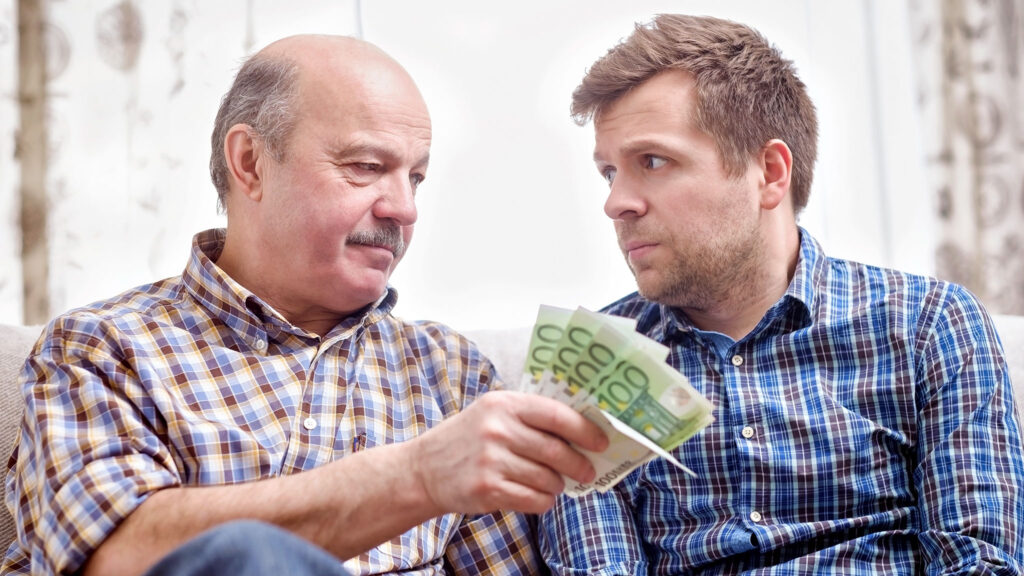 Older man handing cash to his adult son – lending or giving money to family
