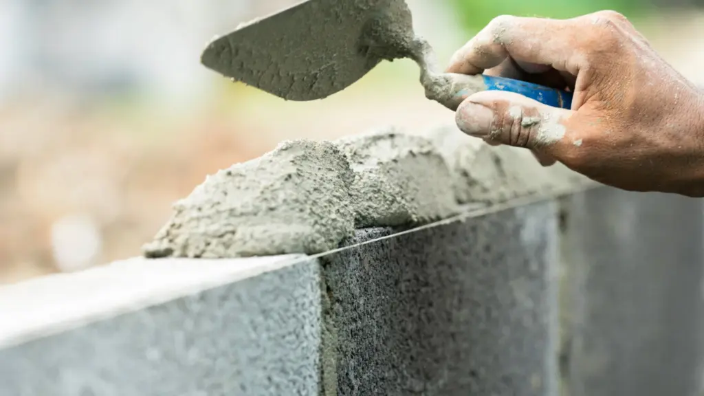 Murarz nakłada zaprawę kielnią na ścianę z bloczków betonowych